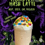 A caramel mocha latte topped with whipped cream and colorful candy, in a mason jar, with Halloween-themed decorations and the text “Monster Mash Latte: Hot, Iced, or Frozen.”.